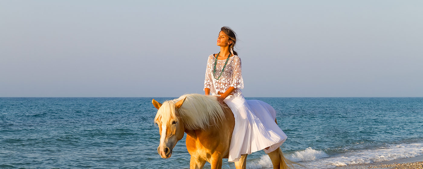 eine Frau genießt die Sonnenstrahlen auf einem Pferd am Strand